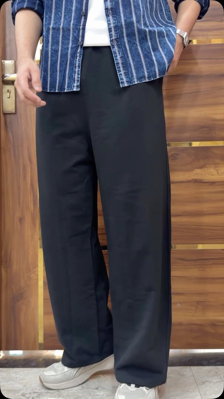 Person wearing black wide-leg track pants with a white t-shirt and blue shirt.