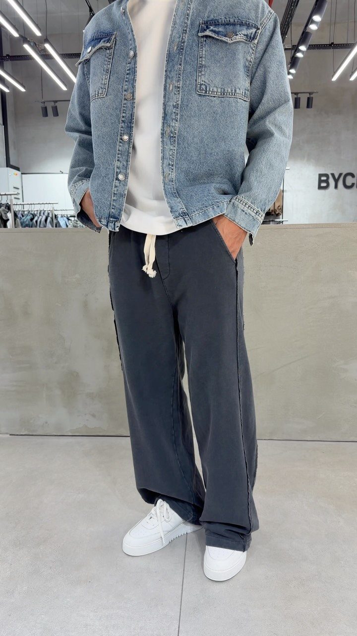 Person wearing a denim jacket, white t-shirt, dark grey track pants, and white sneakers.