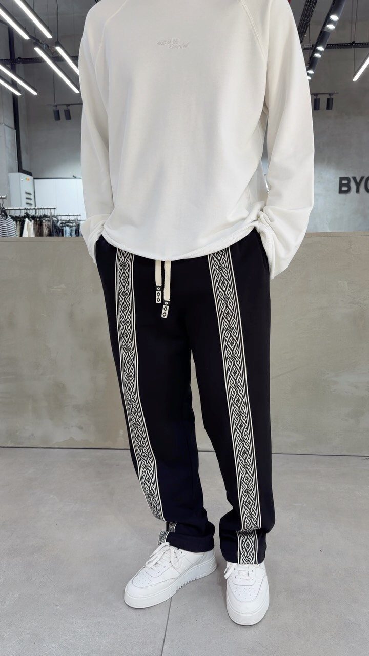 Person wearing white long-sleeved shirt, black patterned track pants, and white sneakers.