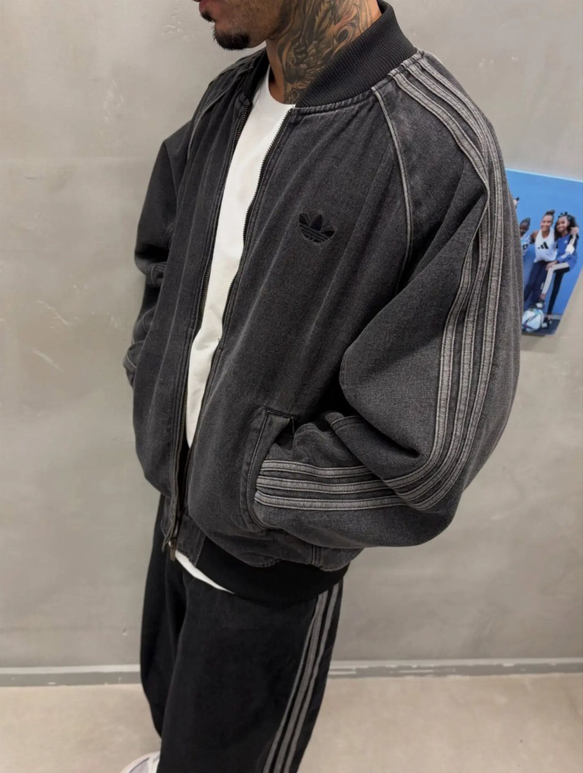 Man wearing black Adidas bomber jacket, white t-shirt, and matching black track pants.