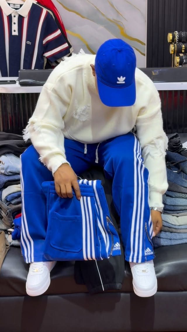 Person wearing a white relaxed-fit sweater and blue striped track pants with sneakers.