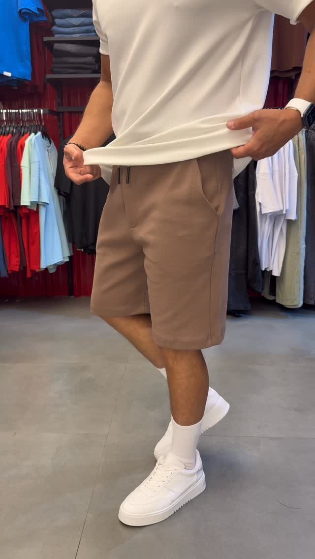 Man wearing tan casual shorts, white t-shirt, and white sneakers in a store.
