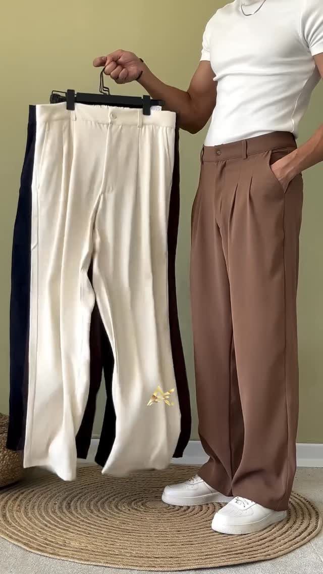 Man wearing brown wide-leg trousers standing next to a rack of colorful pants.