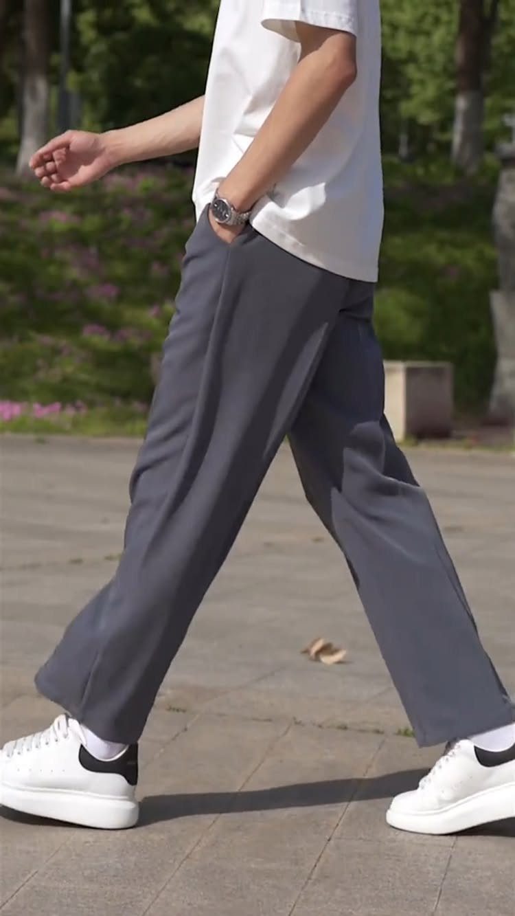 Person walking in wide-leg grey trousers, white t-shirt, and white sneakers outdoors.