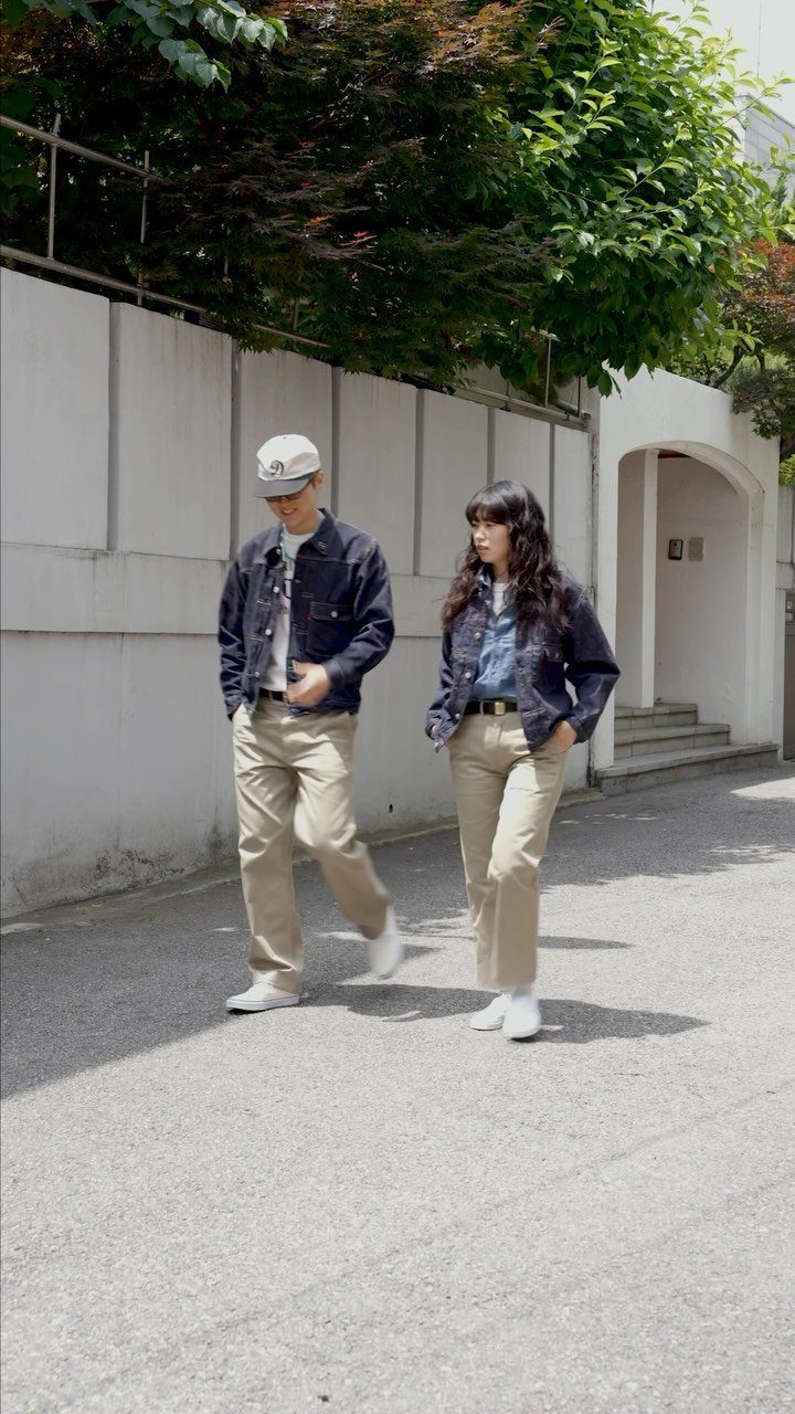 Man and woman wearing tan chinos and dark denim jackets walking outdoors.