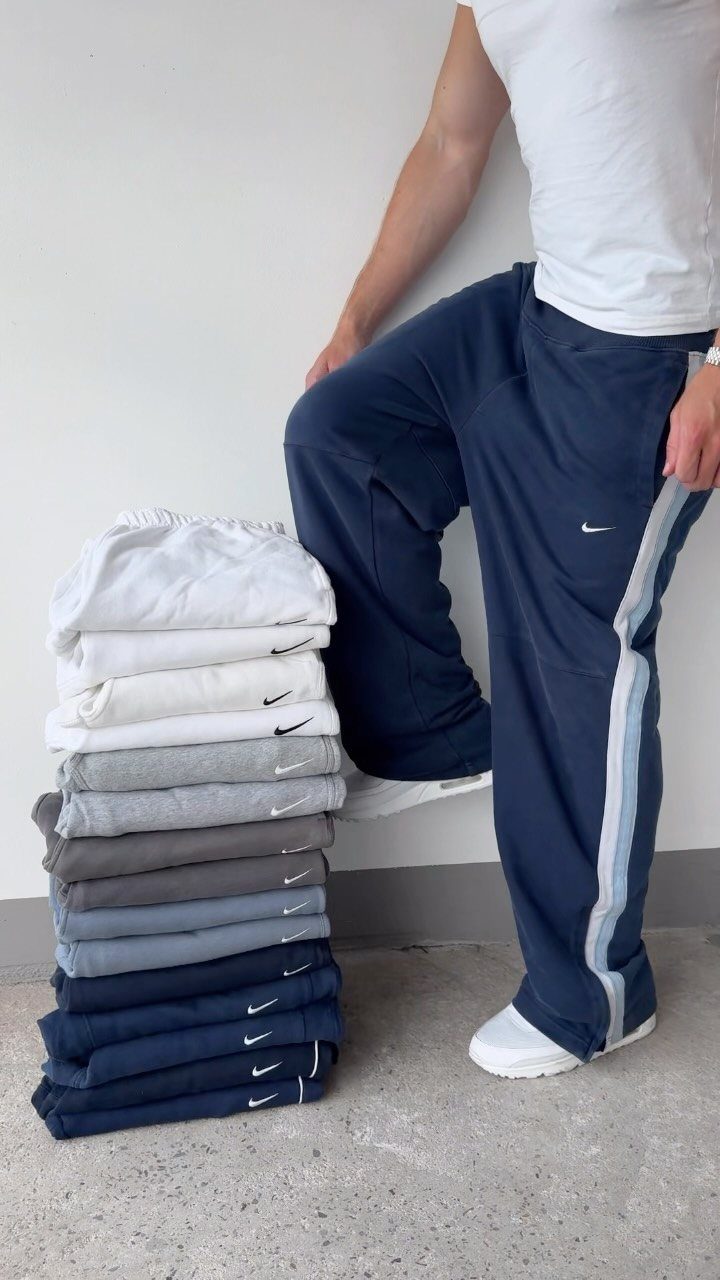 Navy blue athletic pants worn by a person next to a stack of pants.
