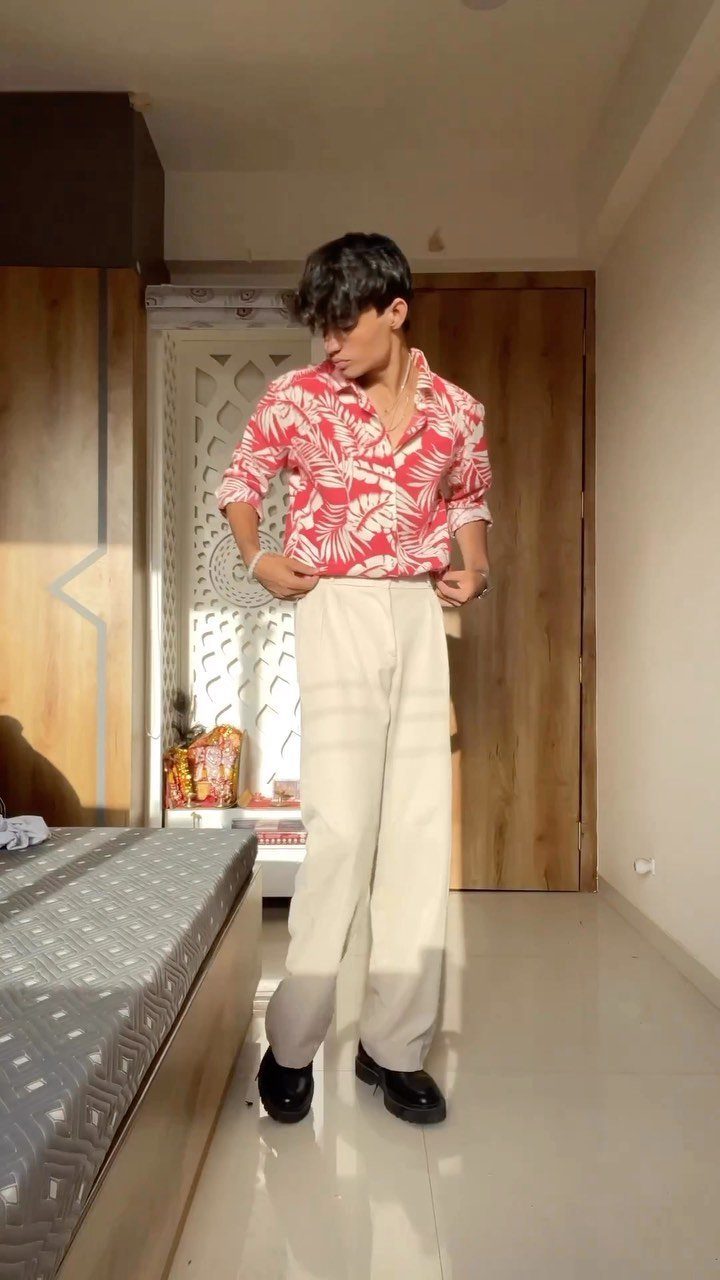 Person wearing a red floral shirt and cream relaxed fit pants in a room.