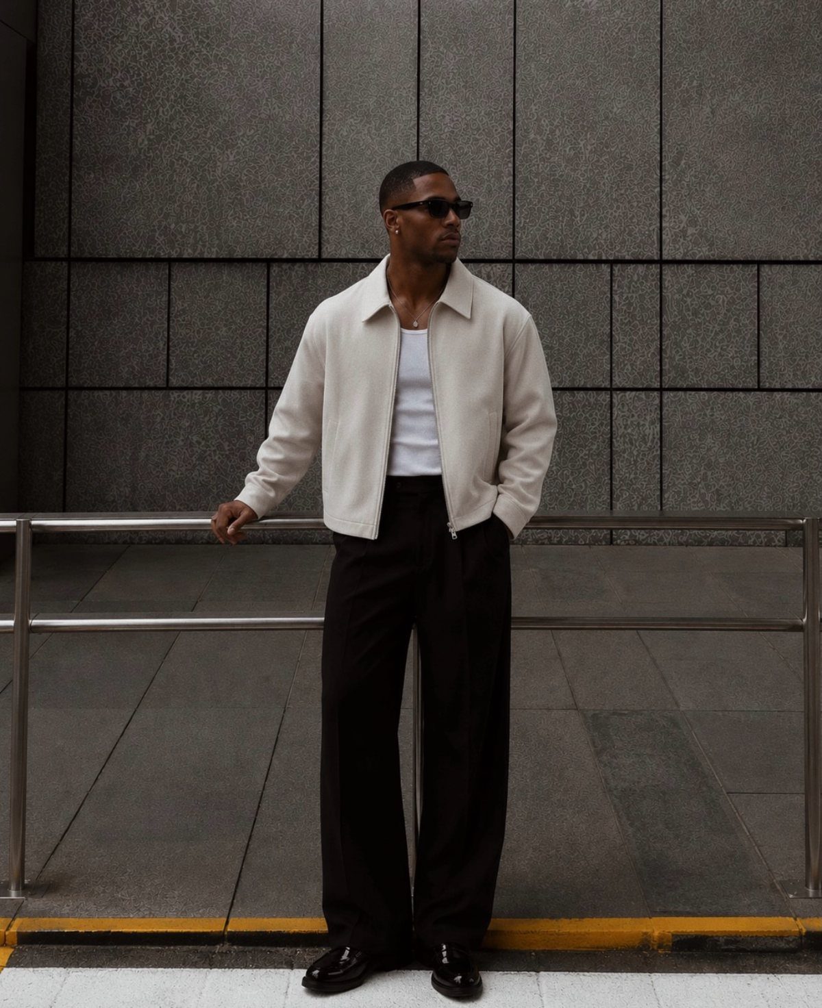 Man wearing a white jacket and black wide-leg trousers standing by a wall