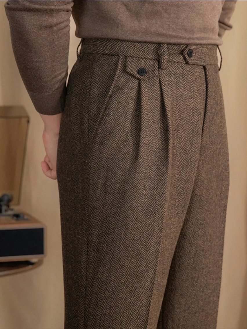 Brown herringbone wool trousers with pleats worn with a matching brown sweater.