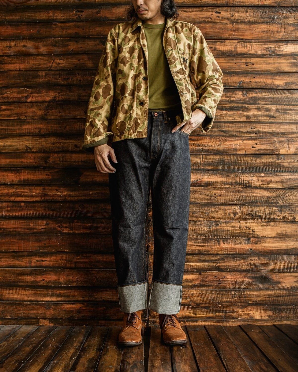 Person wearing high-rise dark denim jeans with wide cuffs and a camouflage jacket.