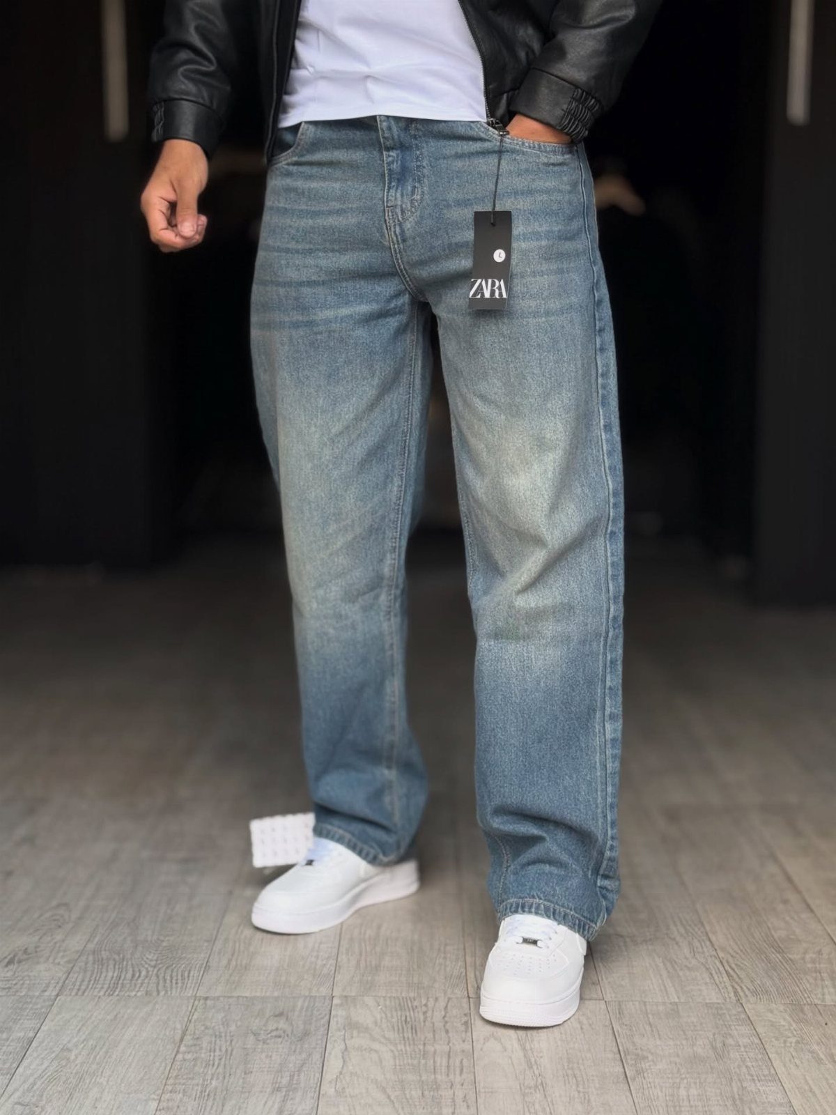 Light-wash relaxed-fit blue jeans worn with a black leather jacket and white sneakers.
