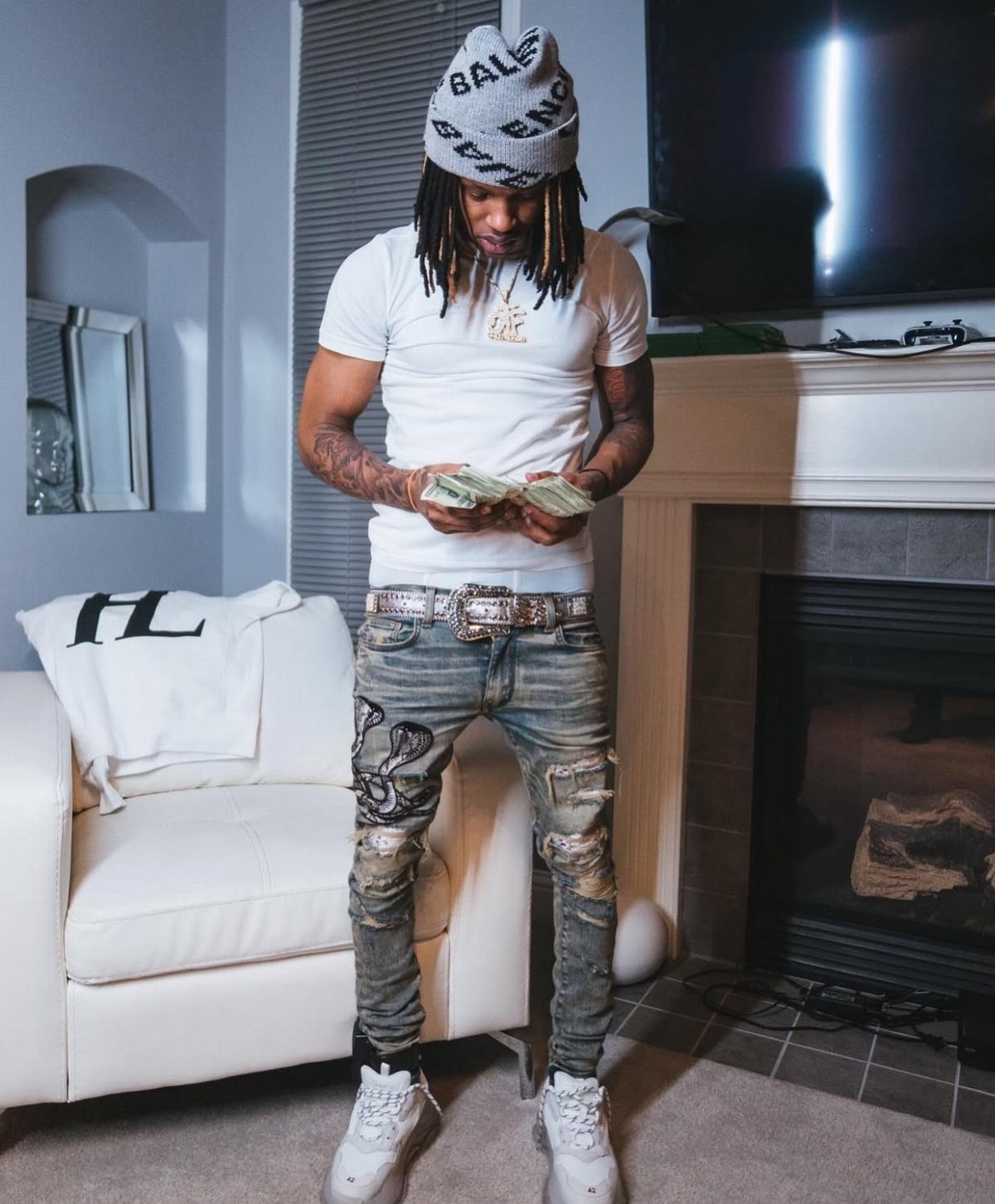 Man in grey distressed slim-fit jeans and white t-shirt holding cash indoors.