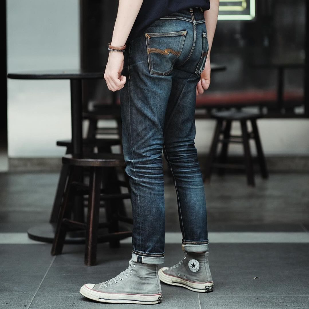 Person wearing dark blue slim-fit denim jeans and grey high-top sneakers outdoors.