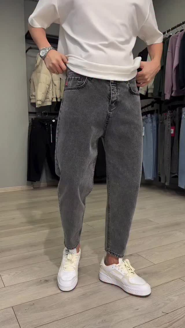 Person wearing grey tapered denim jeans with white sneakers in a clothing store.