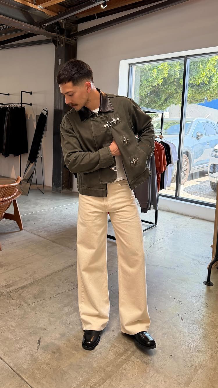 Man in olive green jacket and wide-leg cream trousers standing in a store