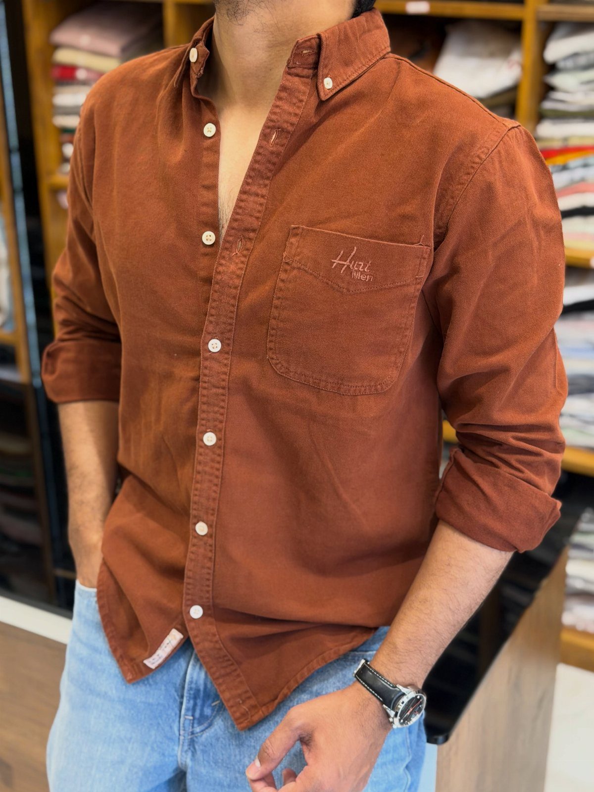 Man wearing a rust-colored button-down shirt and light blue denim jeans.