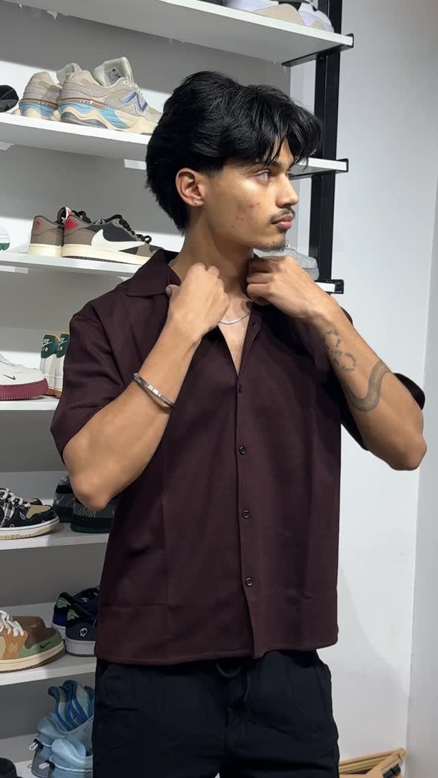 Man wearing a burgundy short-sleeve Cuban collar shirt standing by sneaker shelves.