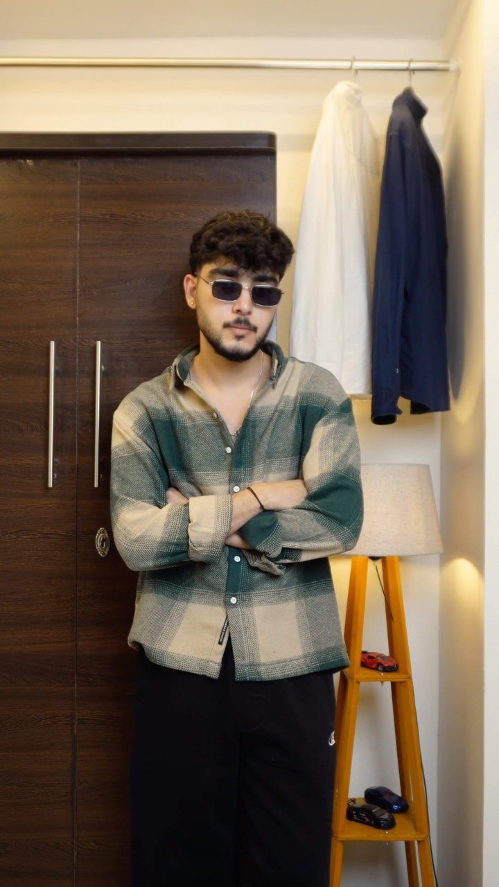 Man wearing a green and beige plaid flannel shirt and sunglasses indoors.