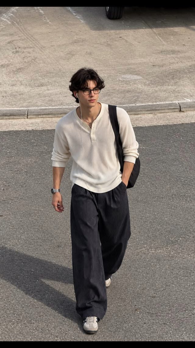 Man wearing a cream henley shirt and dark pinstriped trousers walking on street