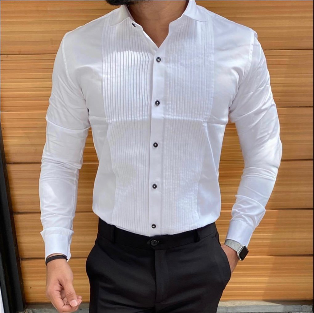 Man wearing a white pleated tuxedo shirt with black buttons and black trousers.