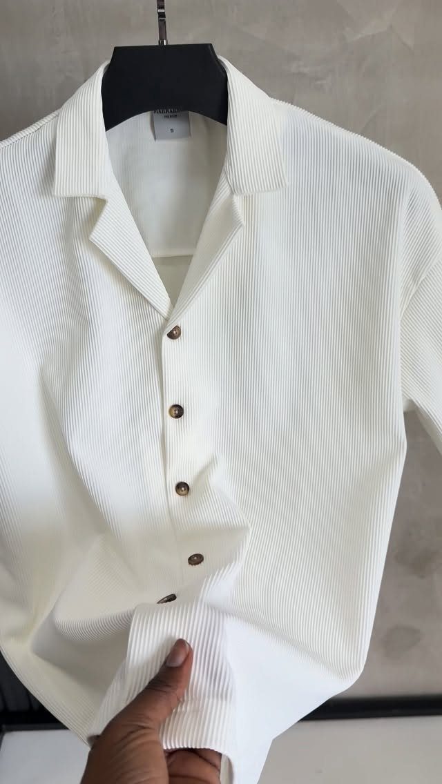 White ribbed short-sleeve button-down shirt hanging on a black hanger against a wall
