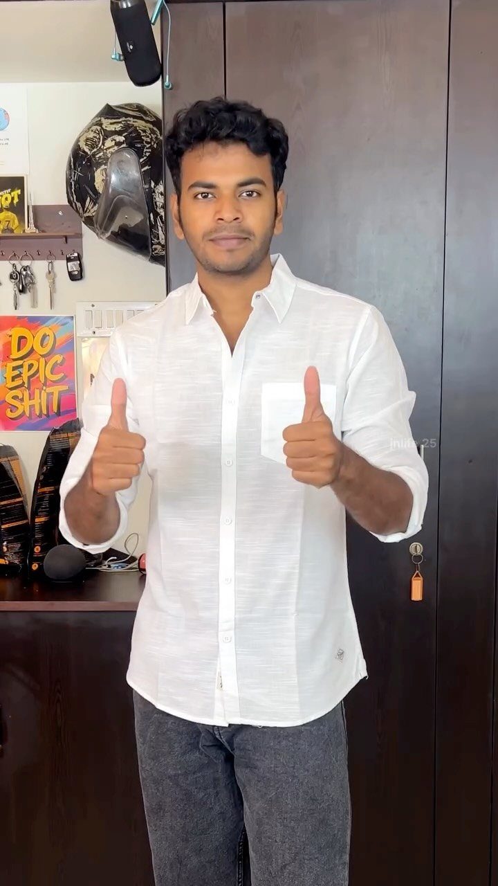 Man wearing a white button down shirt and grey jeans giving two thumbs up.