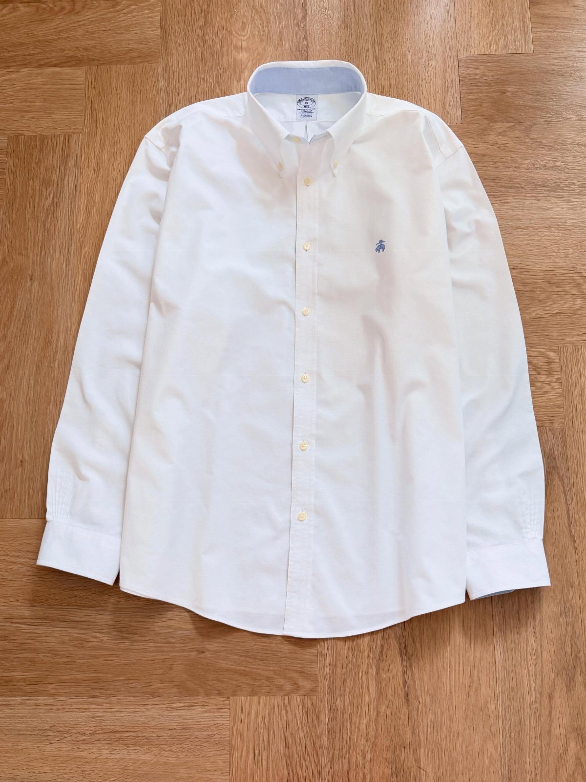 White button-down shirt laid flat on a light brown wooden floor.