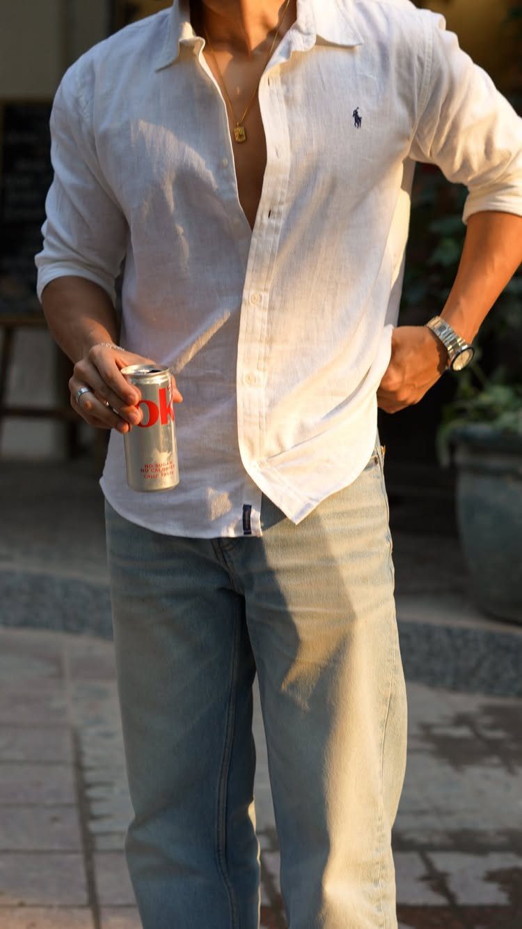 Man wearing a white linen shirt and light blue jeans holding a can
