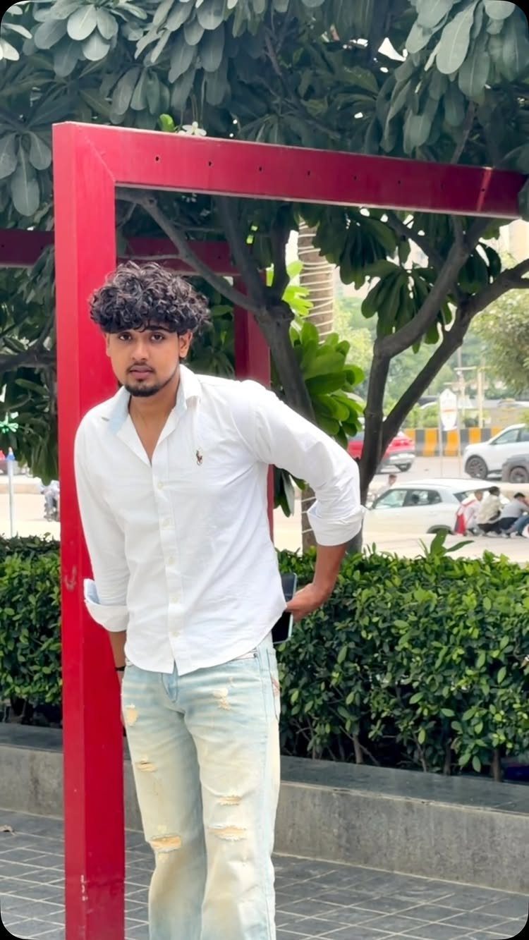 Man wearing a white button-down shirt and light blue distressed jeans posing outdoors.