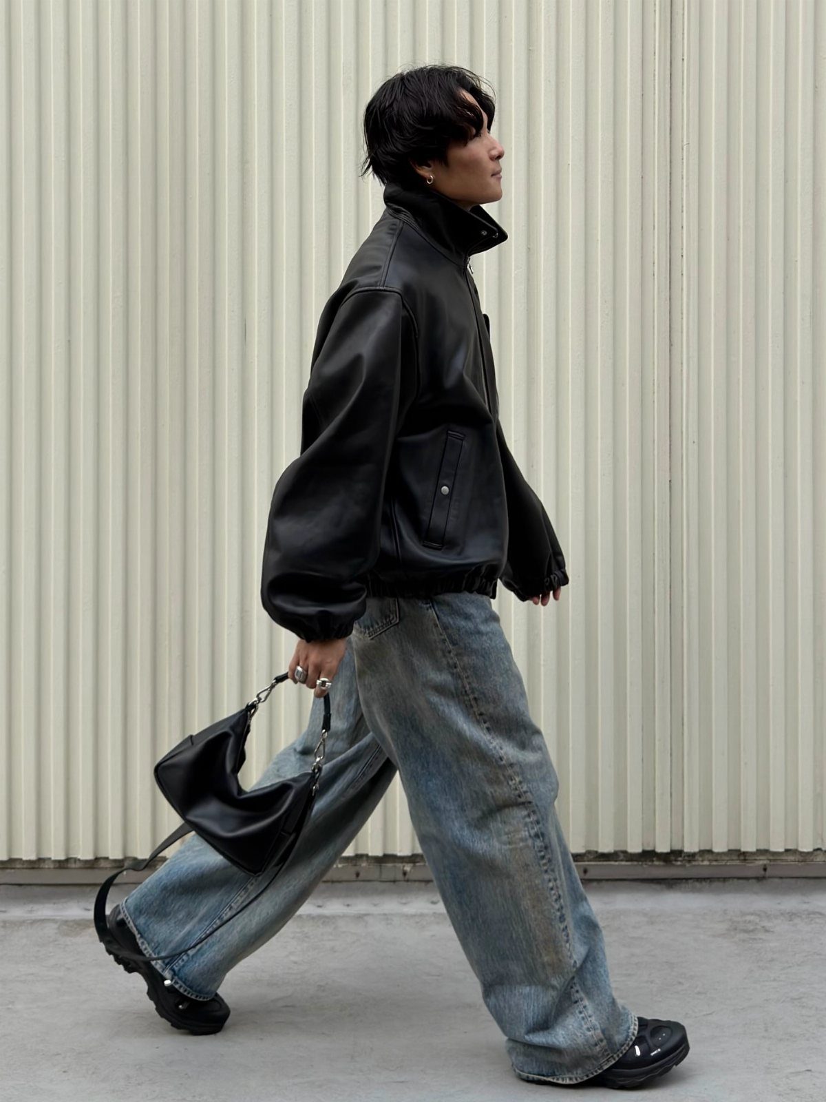 Person wearing a black leather jacket and wide-leg jeans walking outdoors.