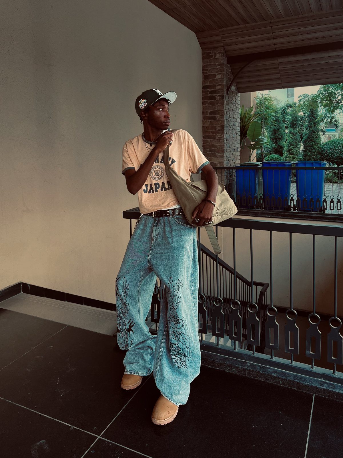 Person wearing light blue wide leg jeans, tan t-shirt, and a baseball cap.