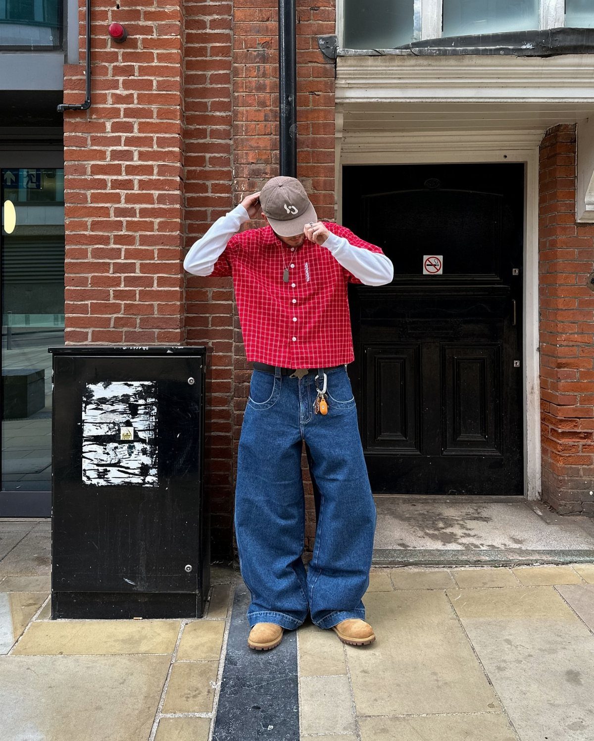 Person wearing wide leg blue jeans, red checkered shirt, and brown baseball cap.
