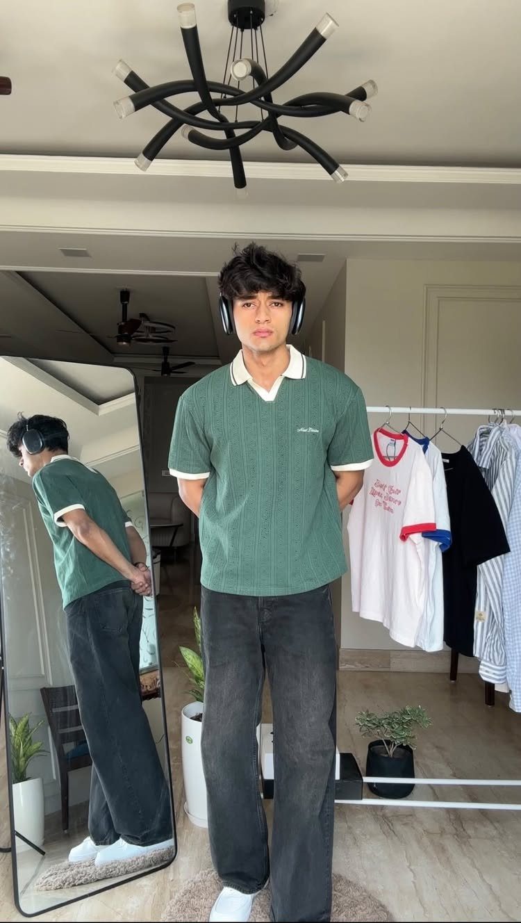 Young man wearing a green polo shirt and dark grey wide leg jeans.