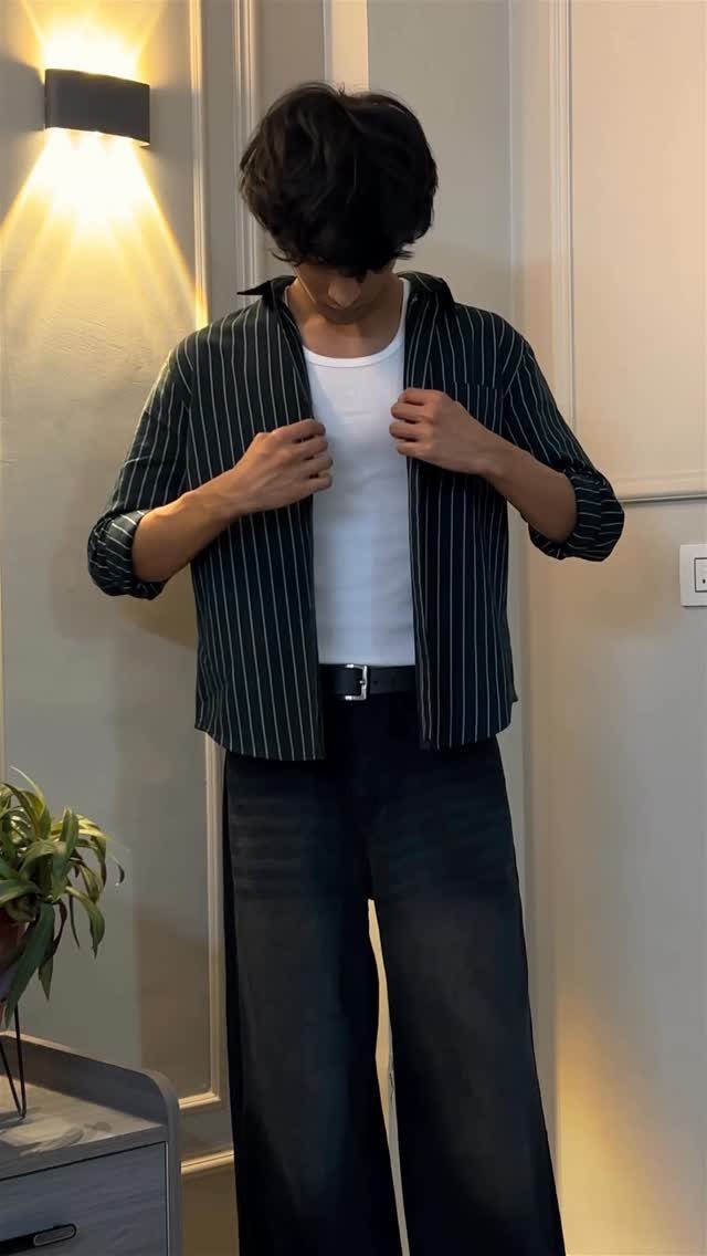 Person wearing a white tank top, open striped shirt, and dark wide-leg jeans.